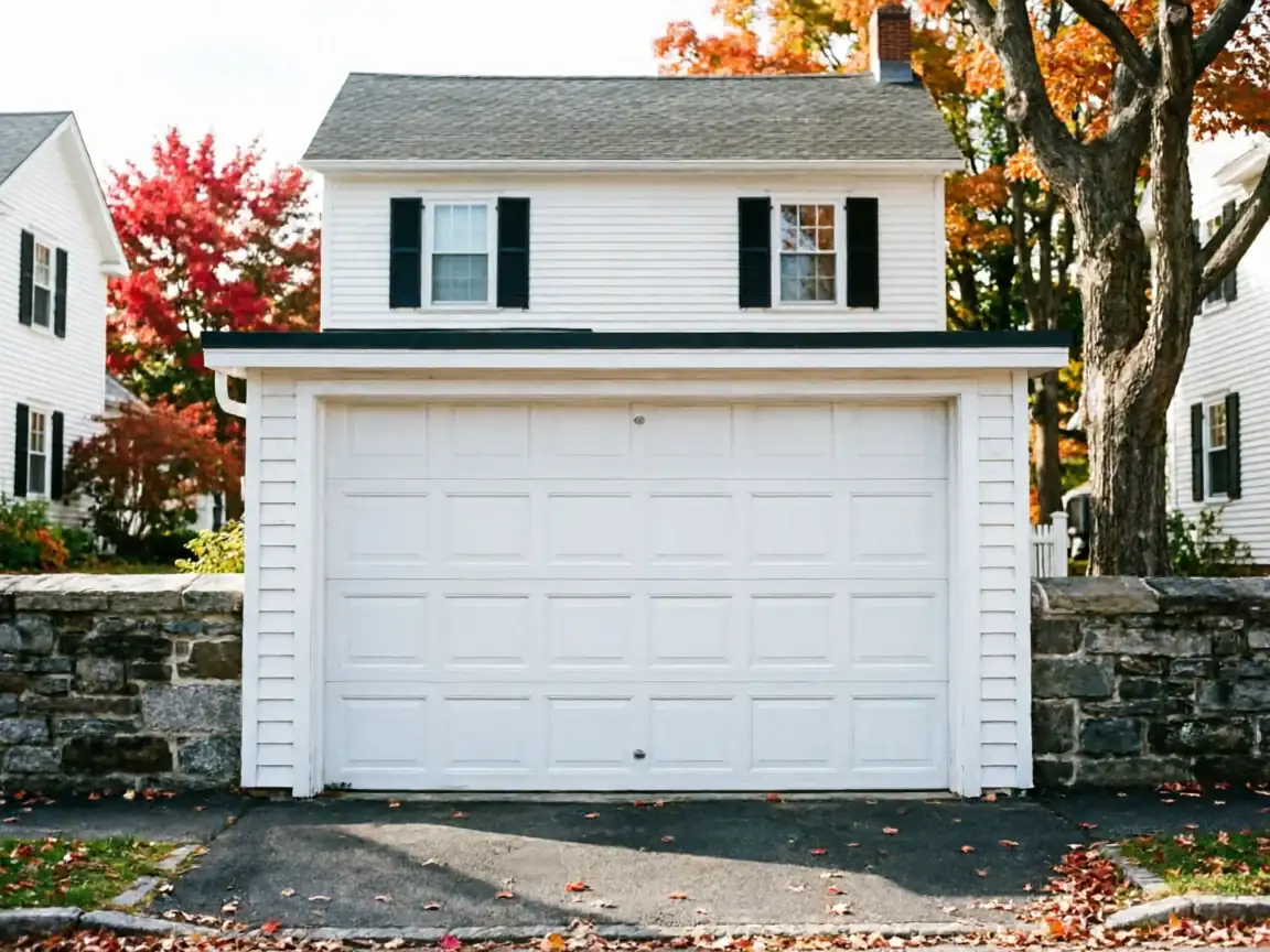 A white garage door on a white house with autumn trees in the background.
